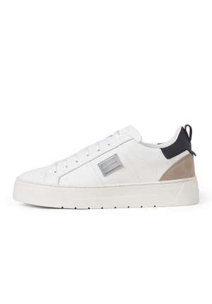 Weißer Sneaker mit niedrigem Schnitt und Schnürung, dicker Sohle, beigem Wildleder-Ferseneinsatz, schwarzer Fersenlasche und silberner Logoplakette an der Seite.