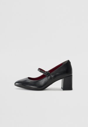Chaussures Mary Jane en cuir noir avec un bout arrondi, une sangle à boucle et un talon bloc de hauteur moyenne. Doublure intérieure rouge. Texture lisse.