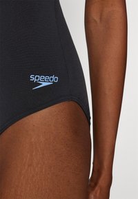 Juodas maudymosi kostiumėlis su lygiu paviršiumi, šone esantis šviesiai mėlynas "Speedo" logotipas. Sukurtas elegantiškam prigludimui, pabrėžiant švarias linijas.