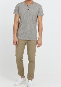Grijs gestreepte short-sleeve henley-shirt met drie knopen, gecombineerd met beige taps toelopende broek en witte sneakers. Eenvoudig ontwerp, casual uitstraling.