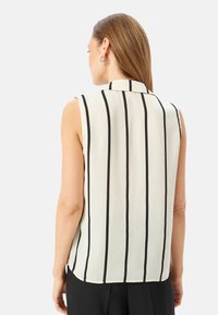 Blusa sin mangas de tejido ligero en color crema con rayas verticales negras, con cuello tipo camisero y dobladillo curvado.
