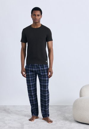 Svart kortärmad t-shirt tillsammans med blå rutig pyjamasbyxa. Tyget verkar mjukt, med en avslappnad passform och bekväm design.