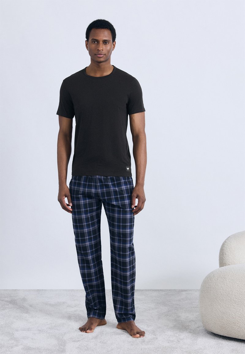 Černé tričko s krátkým rukávem v kombinaci s modrými károvanými pyžamovými kalhotami. Tkanina působí měkce, s uvolněným střihem a pohodlným designem.
