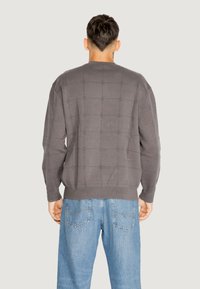 Maglione grigio lavorato a maglia con un motivo a griglia testurizzato, polsini e orlo a coste, indossato con jeans blu.