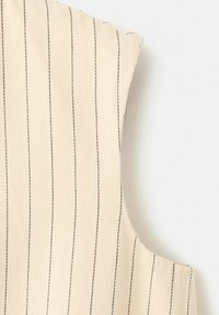 Tissu sans manches de couleur crème avec des fines rayures noires verticales et une subtile texture en chevron sur un fond blanc uni.