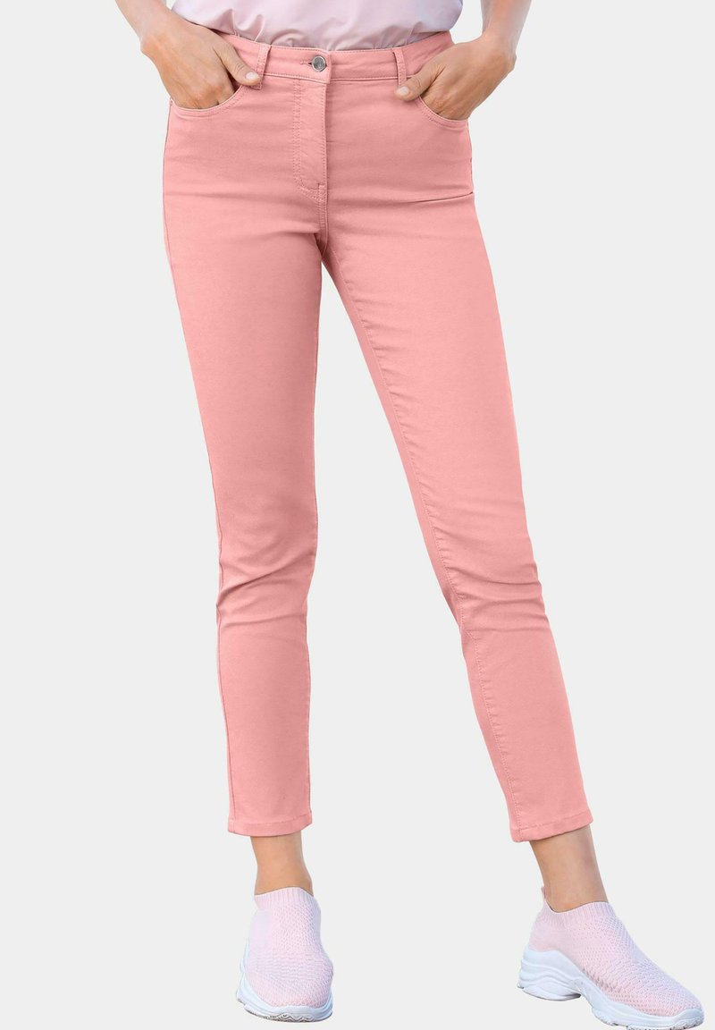 Jeans slim fit rose en denim, avec un design classique à cinq poches et une fermeture à bouton. Accompagnés de baskets blanches.