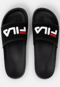 Mustat liukukengät, joissa on puhditettu hihna, jossa valkoinen "FILA"-logo ja punainen yksityiskohta. Pehmeä, teksturoitu pohja mukavuutta varten.