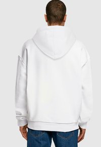 Hvit oversized hettegenser med snor i hetten, ribbede mansjetter og kant. Myk stofftekstur og stikkingdetaljer, båret over blå jeans.