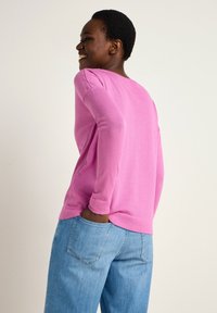 Rosa Langarm-Oberteil aus weichem Stoff, mit rundem Ausschnitt und gemanschten Ärmeln, kombiniert mit hellblauen Jeans.