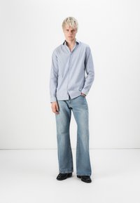 Gestreifte, hellblaue und weiße Button-up-Bluse, kombiniert mit locker sitzenden, hellblauen Jeans und schwarzen Schuhen. Einfaches, lässiges Design.
