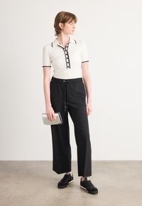 Witte geribde polo met zwarte accenten, zwarte wijde broek, zwarte sneakers en een zilveren clutch. Eenvoudig ontwerp met knopen en een trekkoord.