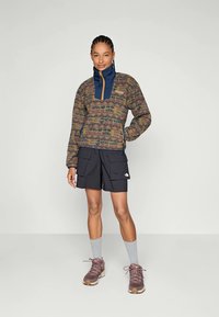 Brun mønstrede pullover med blå krave, parret med sorte cargo-shorts. Brun sneakers og grå sokker fuldender outfittet.
