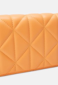 Pomarańczowa pikowana kopertówka ze skóry z detalem przeszyć w kształcie diamentów na jednolitym białym tle.