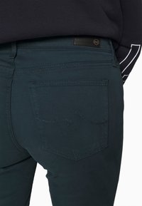 Dunkelblaue Denim-Jeans verfügen über eine Gesäßtasche mit gewelltem Steppdetails und einem Leder-Logopatch. Leicht strukturiertes Material mit tailliertem Design.