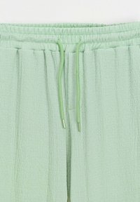 Pantalons texte vert clair avec une taille élastique, comportant un cordon de serrage pour l'ajustement et des détails de coutures verticales sur les jambes.