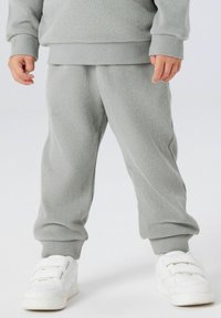 Szare prążkowane spodnie dresowe o luźnym kroju, z elastycznymi ściągaczami oraz dopasowaną szarą bluzą, zestawione z białymi sneakersami na rzepy.