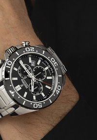 Orologio in acciaio inossidabile argentato con quadrante rotondo nero, indicatori bianchi a contrasto, tre sub-quadranti e display della data. Bracciale e lunetta nera e argentata.