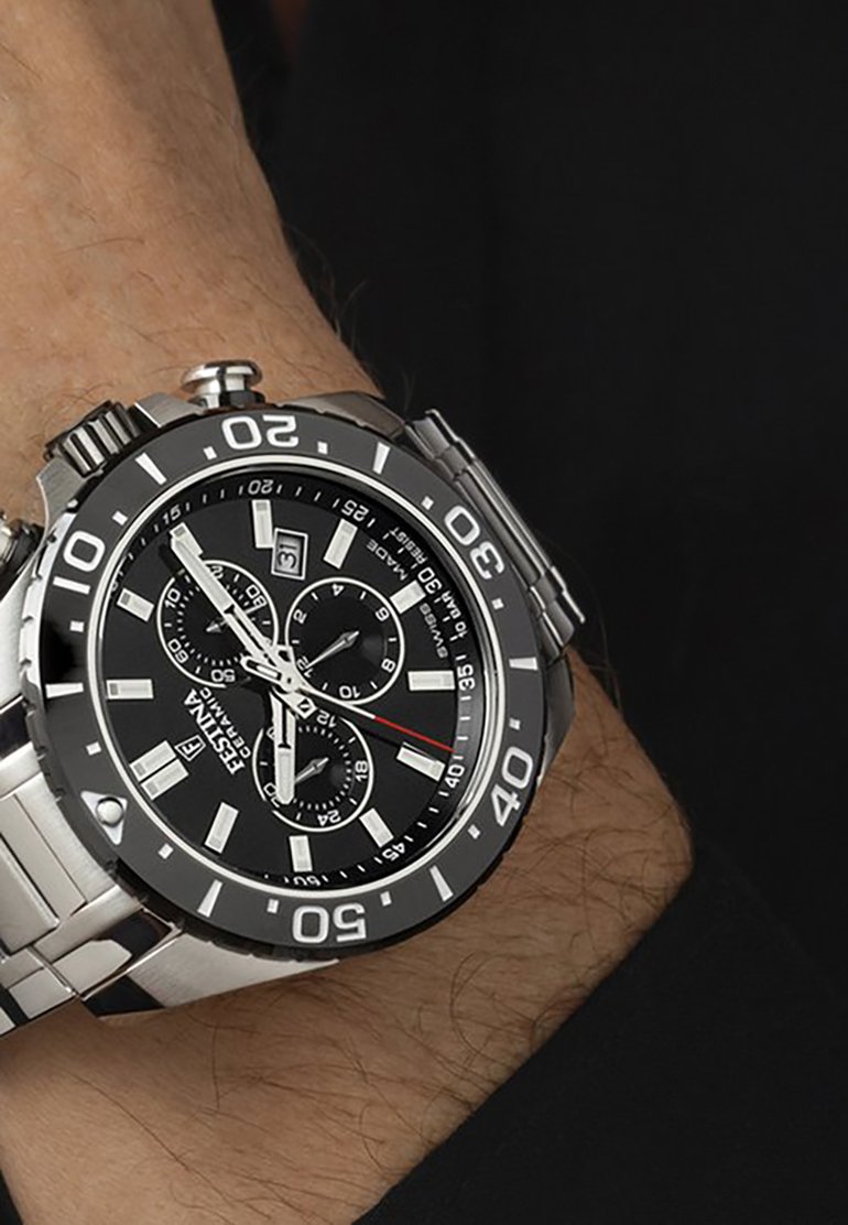 Orologio in acciaio inossidabile argentato con quadrante rotondo nero, indicatori bianchi a contrasto, tre sub-quadranti e display della data. Bracciale e lunetta nera e argentata.