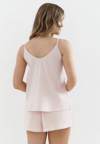 Jasnoróżowa bezrękawnik z koronkowym wykończeniem przy dekolcie, połączony z szortami w kratę z falbaniastymi brzegami. Materiał bawełniany.