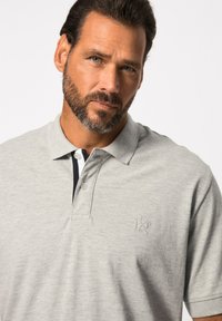 Polo gris avec une patte de boutonnage à trois boutons, un col en marine et un tissu texturé. Présente un logo en relief discret sur la poitrine.
