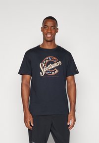 Tamsiai mėlynos spalvos medvilninė marškinėlių su daugi spalve "Sportswear" grafiką ir apvaliu kaklu, derinami su juodomis šortais.
