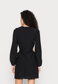 Vestido preto com mangas longas, tecido texturizado, cintura ajustada, recortes laterais e fecho nas costas. Barra lisa e volume subtil nas mangas.