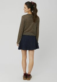 Pull en tricot pailleté bronze avec une coupe courte, associé à une jupe évasée bleu marine parsemée de taches dorées. Des chaussures à plateforme marron complètent le look.