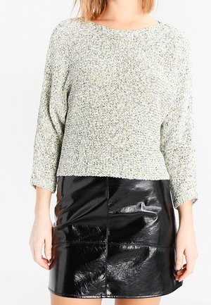 Mujer con un suéter de punto texturizado gris claro de manga tres cuartos y una minifalda de cuero negro brillante.