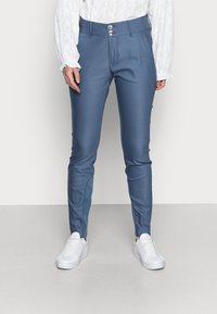 Pantaloni azzurri su misura realizzati in tessuto morbido, caratterizzati da una vestibilità slim, due bottoni frontali e pannelli laterali. Abbinati a sneaker bianche.