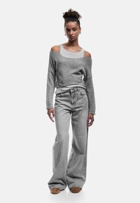 Grauer Pullover mit schulterfreiem Design, kombiniert mit hochgeschnittenen grauen Jeans. Weiche Textur, weit geschnitten und lässige Ästhetik.