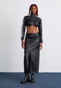 Svart faux skinn cropped jakke med konturdesign, kombinert med et høyt liv svart skjørt med frontslipp og solide svarte platåstøvler.