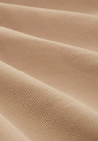 Gros plan sur un tissu beige avec une texture fine et régulière et des plis doux créant des ombres délicates.