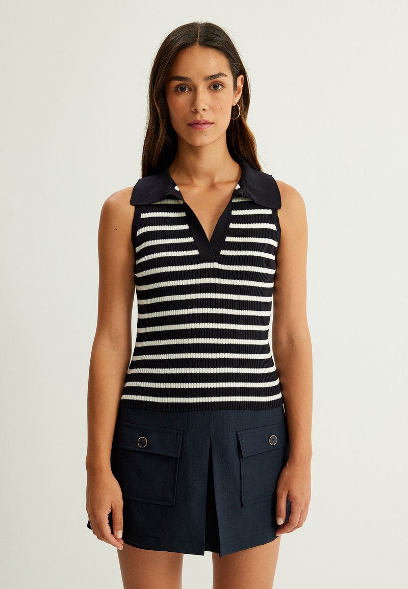 Top senza maniche a righe navy e bianche con colletto a V e texture a coste, abbinato a una skort navy plissettata con tasche frontali.
