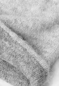 Grijs gebreide stof met een zachte textuur, die een mengsel van lichter en donkerder grijs garen toont en een los geweven patroon heeft.