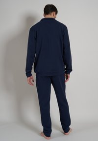Navyblaues Loungewear-Set aus weichem Stoff, bestehend aus einem oberteil mit Kragen und langen Ärmeln sowie passenden Hosen mit elastischem Bund.