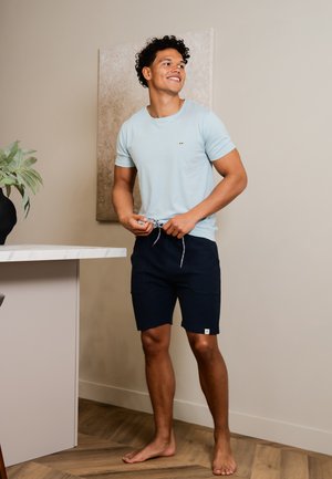Camiseta de manga corta azul clara con un pequeño emblema, combinada con pantalones cortos azul marino con cintura ajustable y bolsillos laterales.
