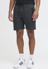 Graue Sportshorts mit einem Zugband an der Taille und schwarzen Reißverschlusstaschen, kombiniert mit weißen Sneakers mit schwarzen Streifen.