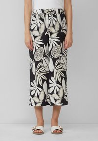 Pantalon large noir avec des motifs de feuilles blanches, taille élastique et texture douce, associé à des sandales blanches avec une boucle décorative.