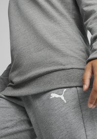 Felpa grigia e pantaloni della tuta realizzati in tessuto morbido, con polsini a coste e un accento del logo bianco sull'anca. Texture liscia in tutto il capo.