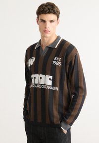 Maglione a righe marrone e blu navy con colletto grigio, caratterizzato da loghi e testo "EST. 1986" e "MORGAAARD COPENHAGEN". Tessuto morbido.