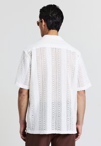Chemise blanche à manches courtes avec un design en dentelle et des rayures verticales, dotée d'un col côtelé. Tissu léger et respirant.
