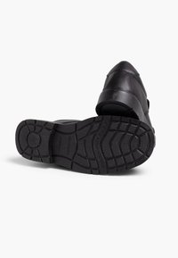 Chaussures en cuir noir avec une semelle en caoutchouc épaisse et texturée. Présente une forme incurvée et des détails de couture le long de la partie supérieure.