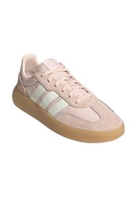 Zapatillas deportivas de color rosa claro con material de gamuza y cuero, que cuentan con tres rayas blancas, una punta redondeada y una suela translúcida beige.