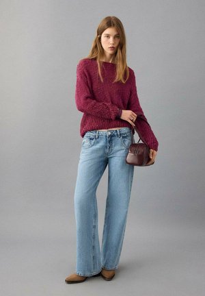 Pulover tricotat texturat bordo, blugi largi bleu deschis și cizme maro până la gleznă, asortate cu o geantă mică maro închis.