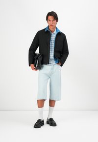 Black jacket, light blue striped shirt, light denim shorts, white socks, and black loafers. Notable details: zip closure, pocket on jacket.