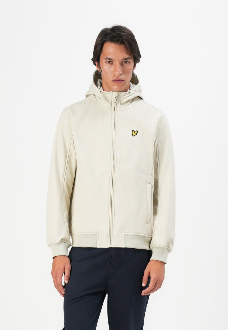 Felpa con zip beige, dotata di tasca frontale e polsini elasticizzati, con un piccolo logo giallo sul lato sinistro del petto. Finitura del tessuto liscia.