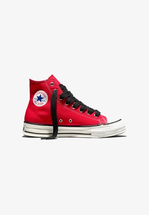 Basket Converse All Star montante rouge avec lacets noirs, semelle en caoutchouc blanche, et patch logo signature sur la cheville. Un lacet est défait.