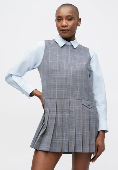 Pelēka kvadrātveida svārku kleita ar krokotām svārku daļām, apaļu apkakli un kabatu uz pleca. Valkāta virs gaiši zilas pogājamas krekla. Gluda tekstūra.