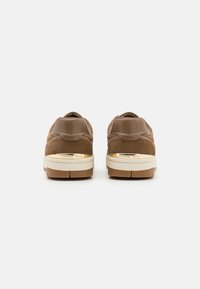 Sneaker in suede marrone con linguetta in pelle beige, suola intermedia crema e suola in gomma. Dettaglio di marca dorato ben visibile sul tallone.