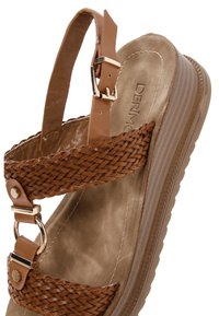 Sandal de cuña marrón con tiras trenzadas, una plantilla suave y acentos de hardware metálico. La suela tiene textura para mayor agarre.